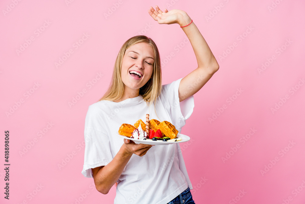 Young russian woman eating a waffle isolated celebrating a special day, jumps and raise arms with energy. Young russian woman eating a waffle isolated celebrating a special day, jumps and raise arms with energy.