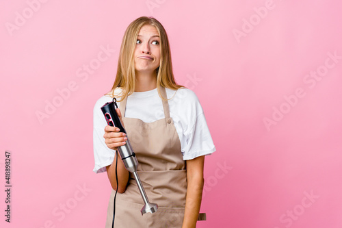 Young russian cook woman holding an electric mixer isolated confused, feels doubtful and unsure.