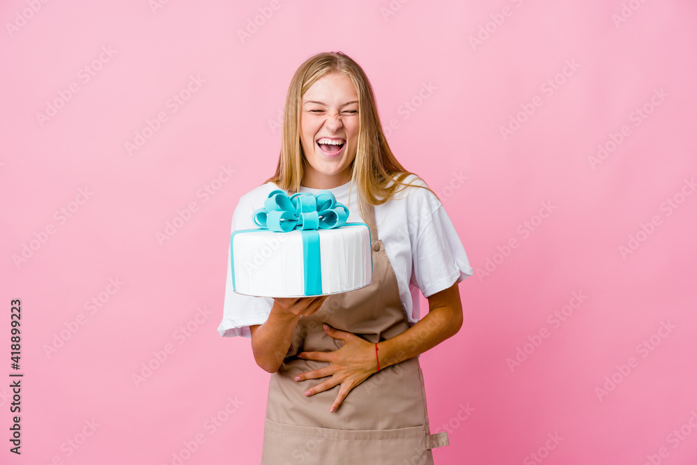 Young russian baker woman holding a delicious cake laughs happily and has fun keeping hands on stomach. Young russian baker woman holding a delicious cake laughs happily and has fun keeping hands on stomach.