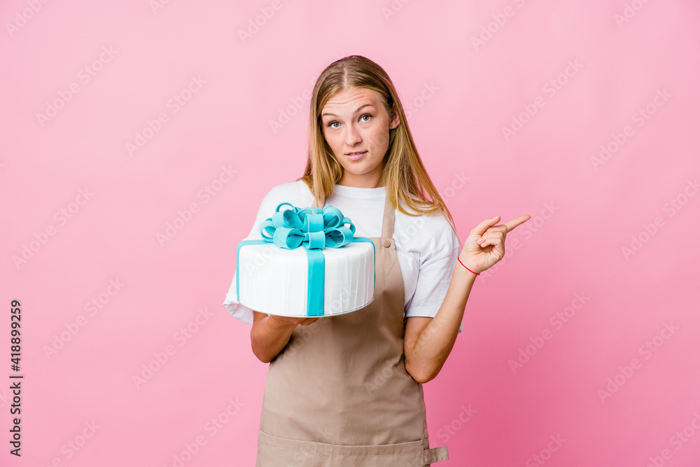 Young russian baker woman holding a delicious cake points sideways, is trying to choose between two options. Young russian baker woman holding a delicious cake points sideways, is trying to choose between two options.