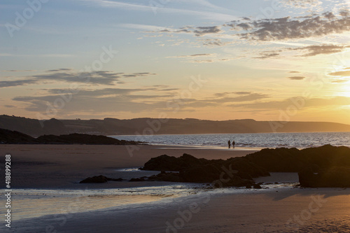 Two people walking their dog on the beach at sunrise