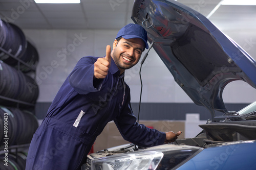 car mechanic standing next to a serviced car WITH A thumbs up 