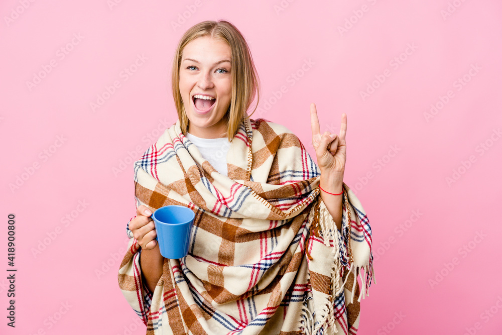 Young russian woman wrapped in a blanket drinking coffee showing a horns gesture as a revolution concept. Young russian woman wrapped in a blanket drinking coffee showing a horns gesture as a revolution concept.
