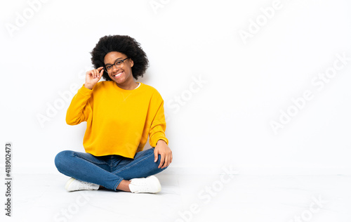 Young African American woman sitting on the floor with glasses and happy © luismolinero