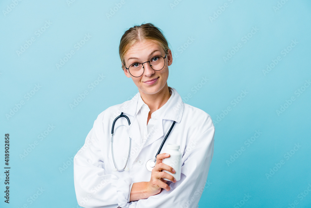 Young russian doctor woman holding pills bottle on blue who feels confident, crossing arms with determination. Young russian doctor woman holding pills bottle on blue who feels confident, crossing arms with determination.