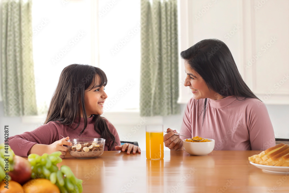 A HAPPY MOTHER AND DAUGHTER LOOKING AT EACH OTHER WHILE EATING BREAKFAST A HAPPY MOTHER AND DAUGHTER LOOKING AT EACH OTHER WHILE EATING BREAKFAST