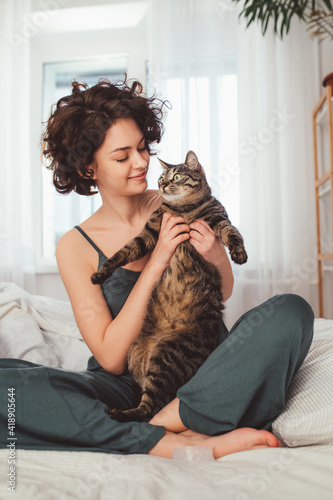 Woman playing with cat in home while sitting at the bed at the bedroom