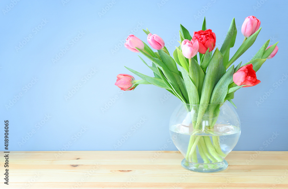 Obraz premium spring bouquet of red and pink tulips flowers in the glass vase over wooden table