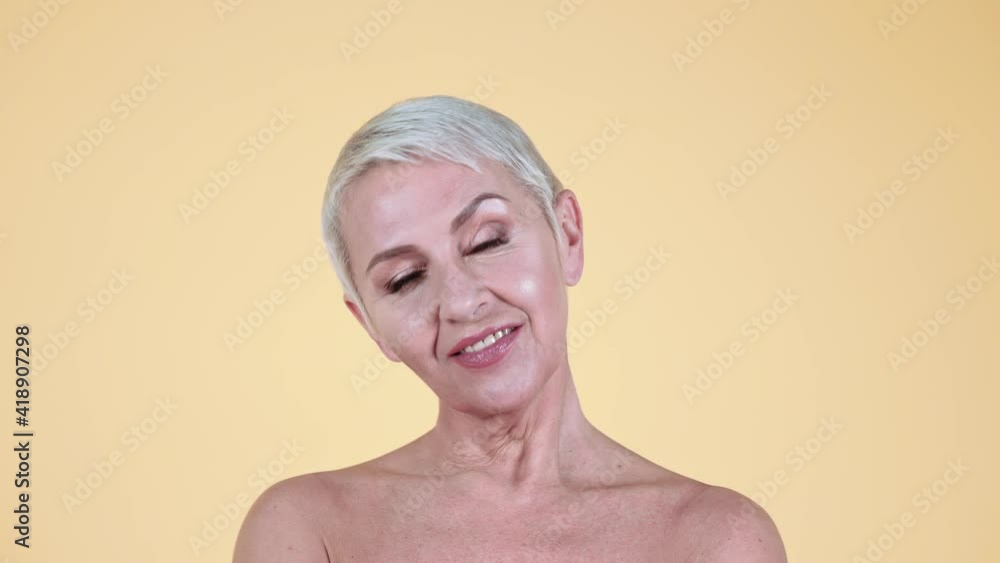 Mature woman with bare shoulders smiling against yellow background Mature woman with bare shoulders smiling against yellow background