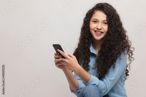 A HAPPY TEENAGER LOOKING AT CAMERA WHILE USING MOBILE PHONE 