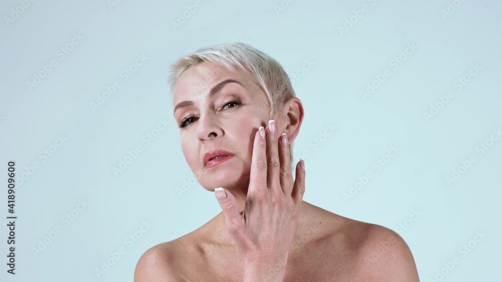 Mature woman touching her face against blue background Mature woman touching her face against blue background