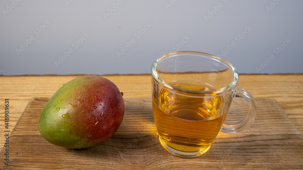 a whole mango with a transparent cup of tea on an eco wooden board. Vegetarian breakfast - top view a whole mango with a transparent cup of tea on an eco wooden board. Vegetarian breakfast - top view