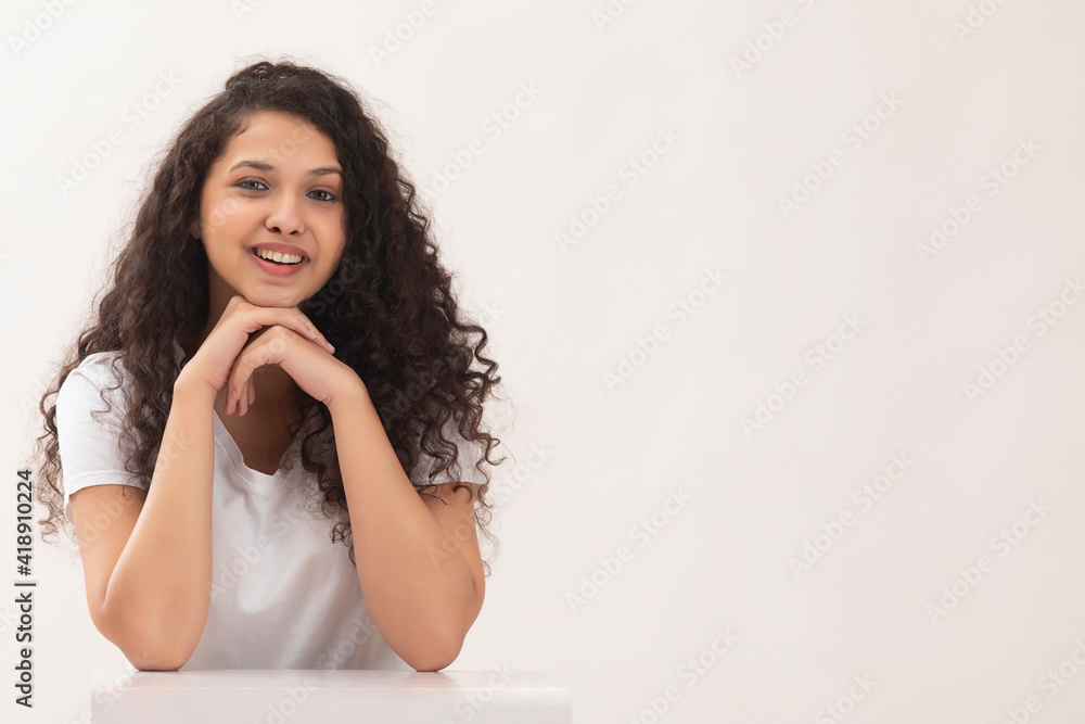 A CURLY HAIRED TEENAGE GIRL SITTING AND HAPPILY POSING IN FRONT OF CAMERA A CURLY HAIRED TEENAGE GIRL SITTING AND HAPPILY POSING IN FRONT OF CAMERA