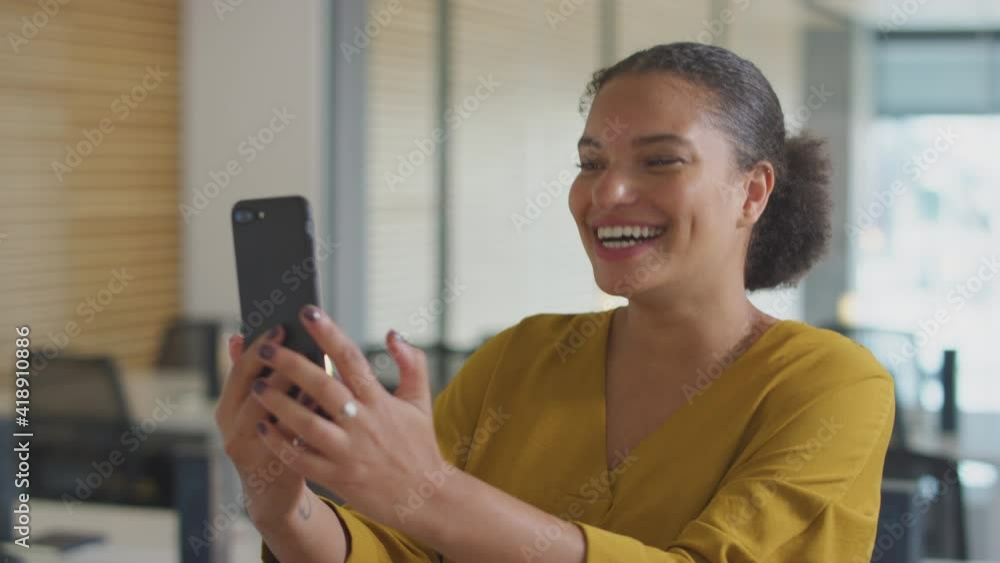 Casually dressed young businesswoman having video chat on mobile phone call in modern open plan start up office - shot in slow motion Casually dressed young businesswoman having video chat on mobile phone call in modern open plan start up office - shot in slow motion