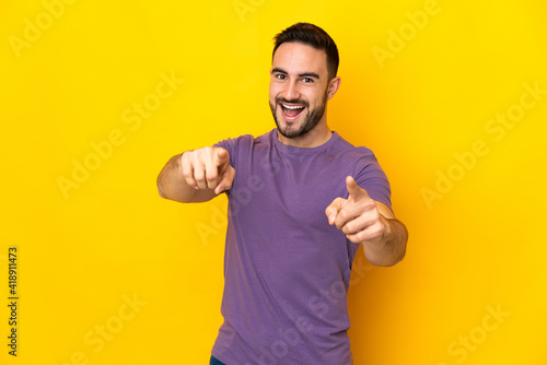 Young caucasian handsome man isolated on yellow background pointing front with happy expression