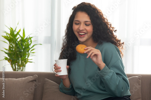 A HAPPY TEENAGER EATING BISCUIT WITH TEA WHILE SITTING AT HOME	 photo