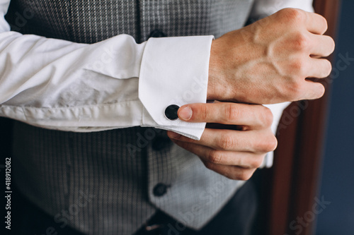 Wedding. The groom. Business. A young man in a white shirt and vest straightens cufflinks on his sleeves