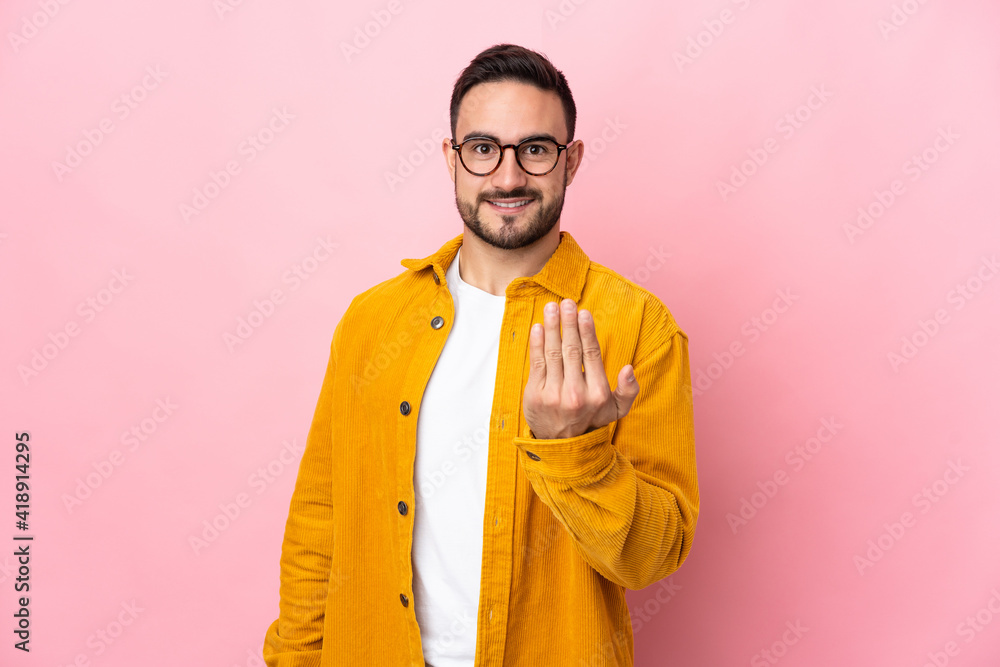 Fototapeta premium Young caucasian handsome man isolated on pink background inviting to come with hand. Happy that you came