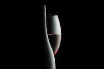 Elegant red wine glass and a wine bottles in black background