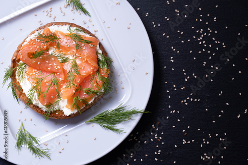 appetizing half of a bun with smoked fish, fresh cream, sprinkled with dill and sesame seeds