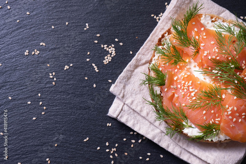 one half bun, oiled with fresh cream, garnished with smoked fish trout and sprinkled with fresh dill and sesame seeds on a napkin on the right side