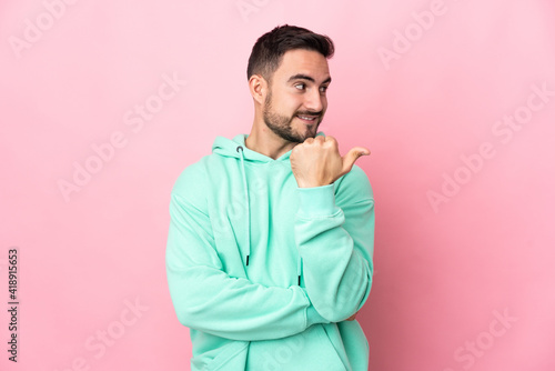 Young caucasian handsome man isolated on pink background pointing to the side to present a product