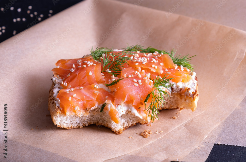 an appetizing, bitten off bun, greased with fresh cream, garnished with smoked fish trout and sprinkled with fresh dill and sesame seeds an appetizing, bitten off bun, greased with fresh cream, garnished with smoked fish trout and sprinkled with fresh dill and sesame seeds