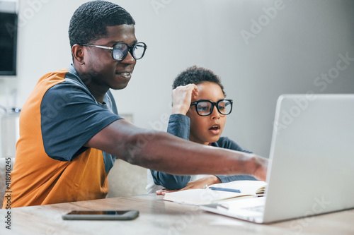 African american father with his son is indoors at home. Using laptop. Conception of education