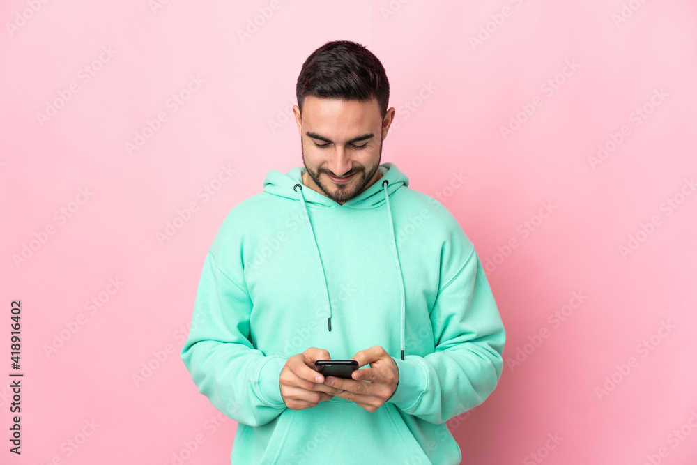 Young caucasian handsome man isolated on pink background sending a message with the mobile Young caucasian handsome man isolated on pink background sending a message with the mobile