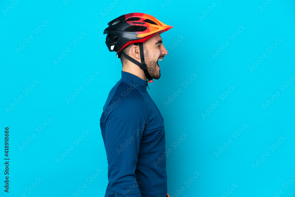 Young cyclist man isolated on blue background laughing in lateral position - obrazy, fototapety, plakaty 