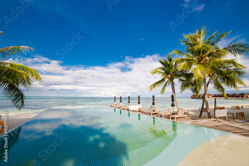 Outdoor tourism landscape. Luxurious beach resort with swimming pool and beach chairs or loungers umbrellas with palm trees and blue sky  sea horizon. Summer island relax travel and idyllic vacation 