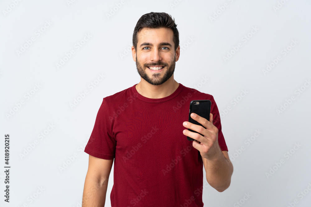 Young handsome man with beard using mobile phone isolated on white background smiling a lot Young handsome man with beard using mobile phone isolated on white background smiling a lot