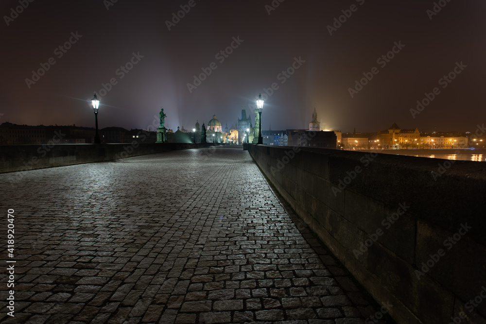 empty sidewalk on the illuminated Charles Bridge at night in the center of Prague