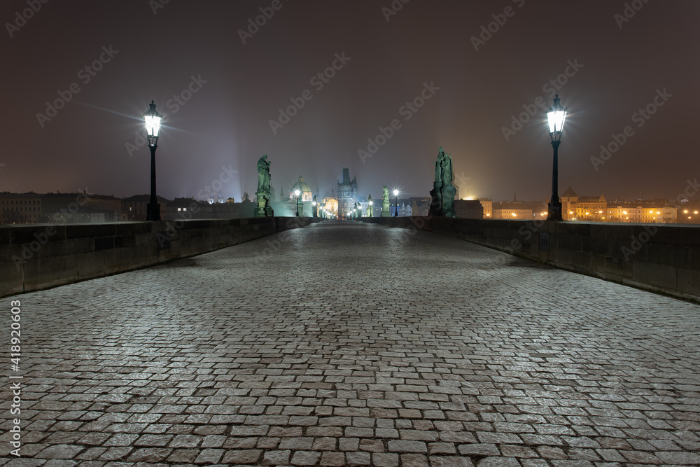 
old stone tower on Charles Bridge at night and St. Vitus Cathedral in the background in the center of Prague at night
