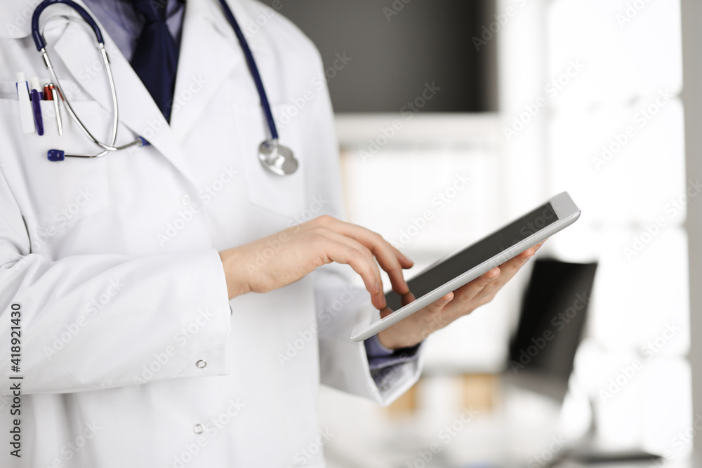 Unknown male doctor using tablet computer in clinic near his working place, closeup. Perfect medical service in hospital. Medicine and healthcare concept Unknown male doctor using tablet computer in clinic near his working place, closeup. Perfect medical service in hospital. Medicine and healthcare concept
