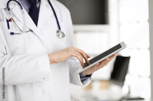 Unknown male doctor using tablet computer in clinic near his working place, closeup. Perfect medical service in hospital. Medicine and healthcare concept