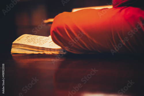 monk with an ancient prayer book while he is reading in the assembly hall of a monastery in Thailand