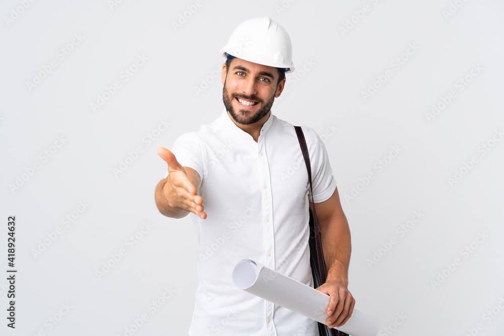 Young architect man with helmet and holding blueprints isolated on white background shaking hands for closing a good deal