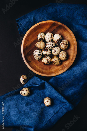 Minimal concept of fresh quail eggs in the wooden bowl on the dark background with blue saten or silk around.