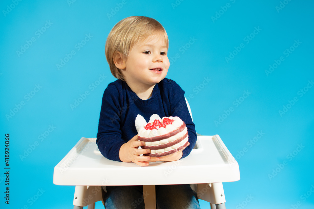Beautiful baby boy sitting holding a cake and smiling over blue background. Beautiful baby boy sitting holding a cake and smiling over blue background.