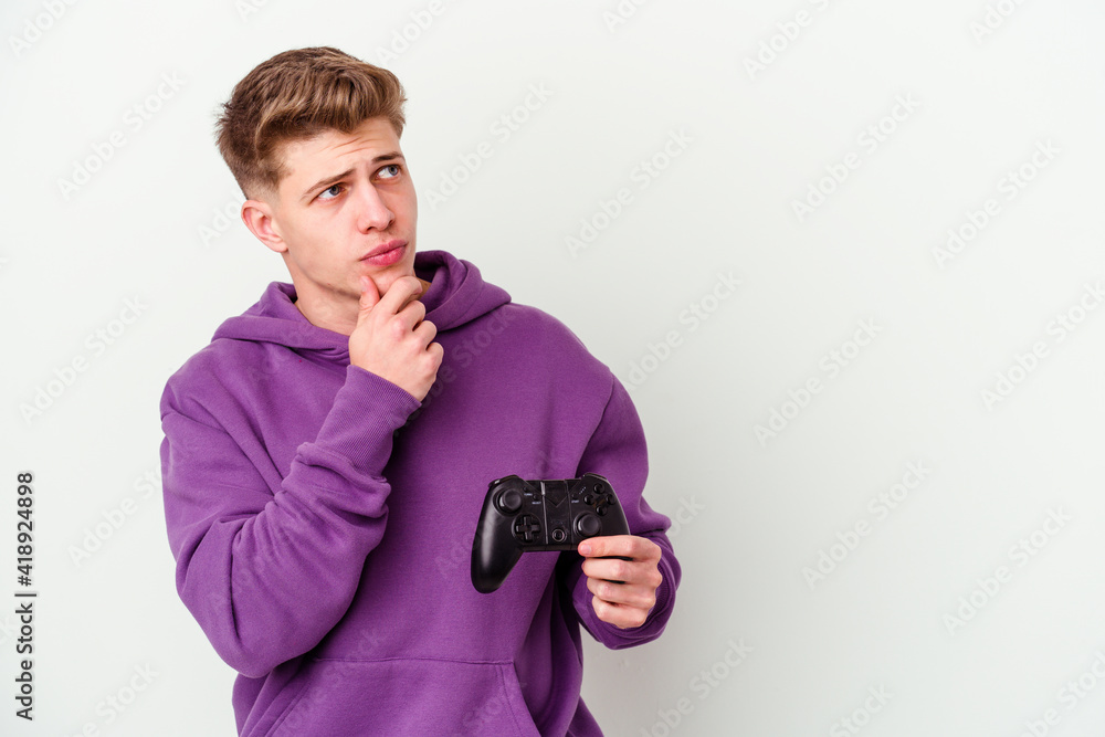 Young caucasian man holding a gamepad isolated on white background looking sideways with doubtful and skeptical expression. Young caucasian man holding a gamepad isolated on white background looking sideways with doubtful and skeptical expression.
