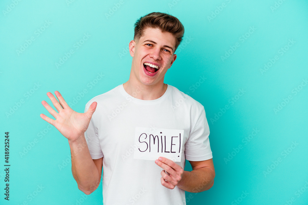 Young caucasian man holding a smile placard isolated on blue background Young caucasian man holding a smile placard isolated on blue background
