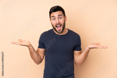 Caucasian handsome man isolated on beige background with shocked facial expression