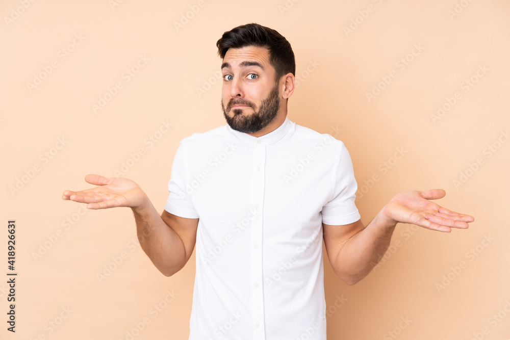 Caucasian handsome man isolated on beige background making doubts gesture Caucasian handsome man isolated on beige background making doubts gesture
