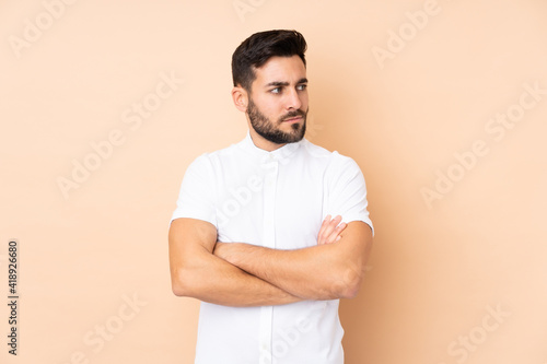 Caucasian handsome man isolated on beige background keeping the arms crossed
