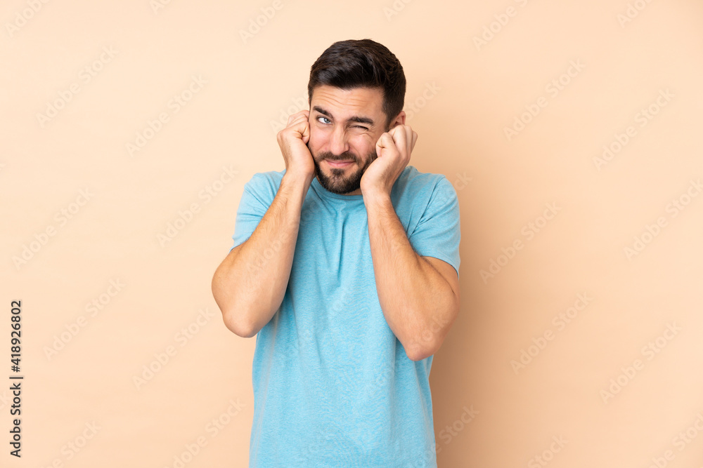 Caucasian handsome man isolated on beige background frustrated and covering ears Caucasian handsome man isolated on beige background frustrated and covering ears