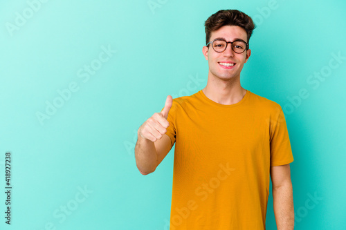 Young caucasian man isolated on blue background smiling and raising thumb up