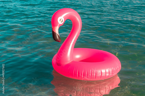 Summer holiday poster. Pink inflatable flamingo in blue ocean water for sea summer beach background. Funny bird toy for kids. © Maksym