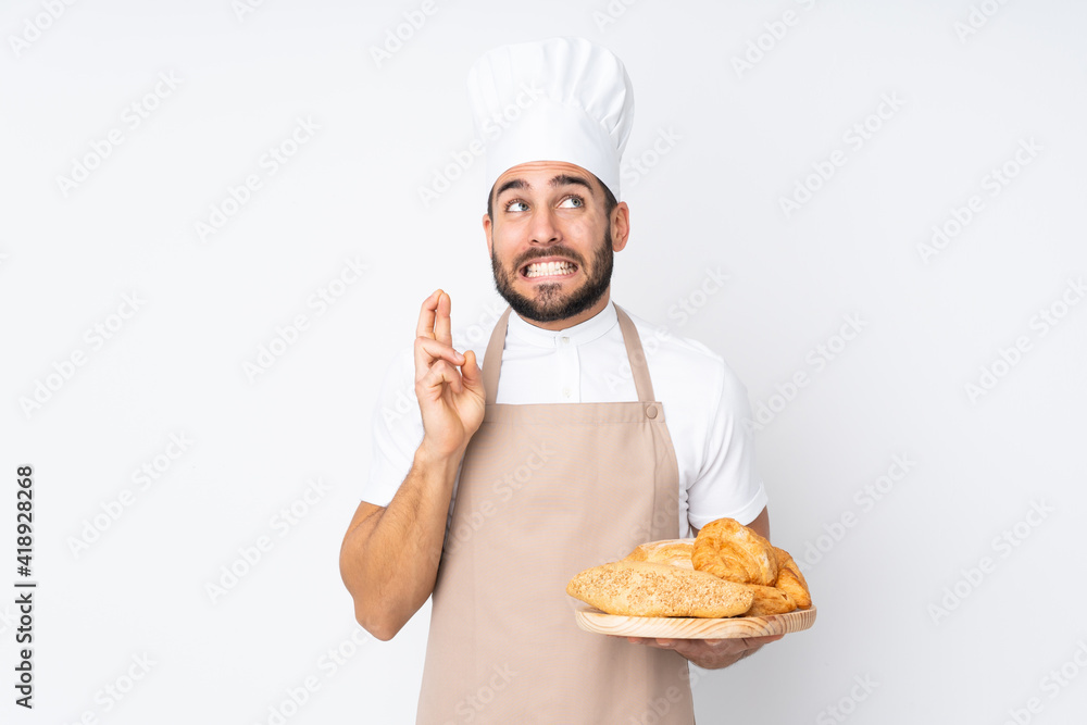 Male baker holding a table with several breads isolated on white background with fingers crossing Male baker holding a table with several breads isolated on white background with fingers crossing