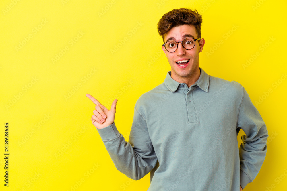 Young caucasian man isolated on yellow background smiling cheerfully pointing with forefinger away. Young caucasian man isolated on yellow background smiling cheerfully pointing with forefinger away.